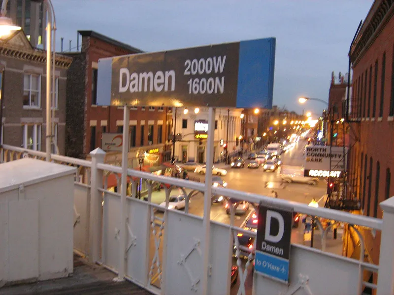 Damen station sign above lit Milwaukee Avenue storefronts at dusk